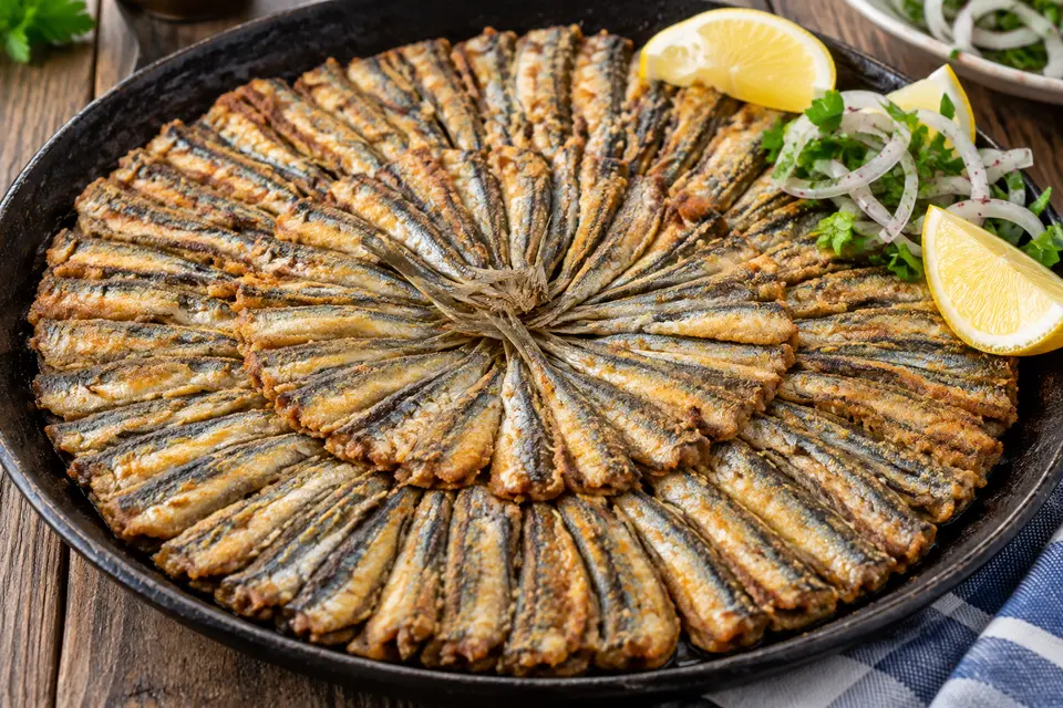 Turkish Hamsi Tava with cornmeal-coated fried anchovies arranged in a golden sunburst, served with lemon and sumac onion salad