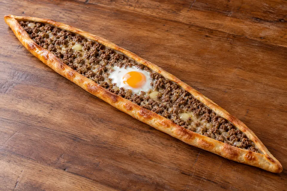 Ordu Pidesi entière, exceptionnellement longue et étroite, aux bords dorés semi-ouverts, garnie de bœuf et d'oignon, de beurre fondu et d'un œuf cuit au centre